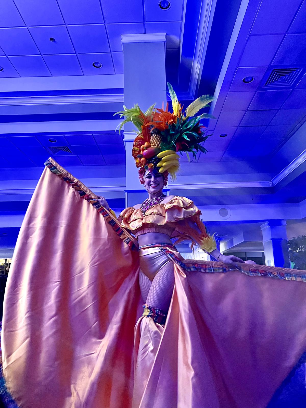 Carnival stilt walker in feathered fruit headdress on the event floor